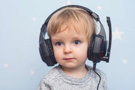 A little pretty child listening to music in headphones. A boy in headphones on a blue background.の写真素材