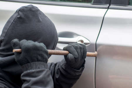 Robber man in black hoodie jacket using a crowbar to break lock and steal a vehicle. Car thief or theft for insurance concept.の写真素材