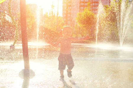 Happy child has fun playing in water fountains on hot day during summer. Boy playing in water at waterpark. A kid in spray park.の写真素材