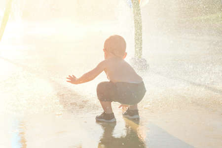 Happy child has fun playing in water fountains on hot day during summer. Boy playing in water at waterpark. A kid in spray park.の写真素材
