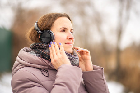 Joyful young woman in jacket listening to music, relaxing in a parkの写真素材