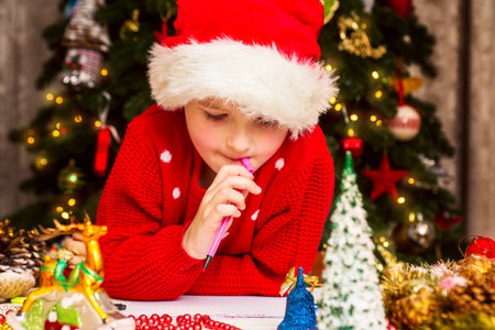 Boy in Santa hat writes letter to Santa Claus near Christmas treeの写真素材