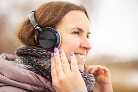 Joyful young woman in jacket listening to music, relaxing in a parkの写真素材