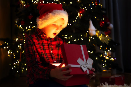 Cute boy opening magic Christmas gift by a Christmas tree. Merry Christmasの写真素材