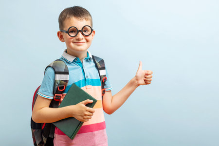 Back to school. Happy elementary school student in eyeglasses hugging bookの写真素材