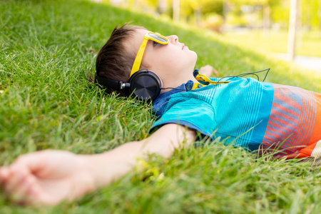 Happy boy in sunglasses lying on grass and listening to music in headphonesの写真素材