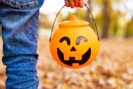 Child holds a bucket shaped like a halloween pumpkin jack o lanternの写真素材