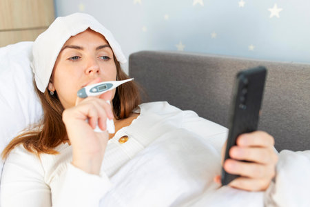 Sick young woman with bad cold, flu or fever holding thermometerの写真素材
