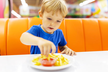 Cute child eating french fries with sauce at table in fast food restaurantの写真素材