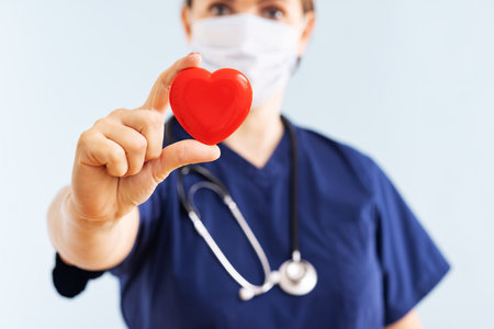 Female doctor with stethoscope holding red heart on blue backgroundの写真素材