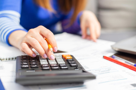 Close up young woman using calculator, managing household monthly budgetの写真素材