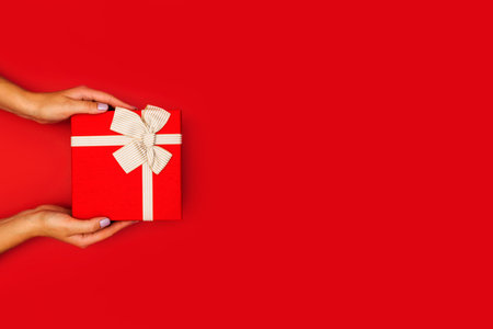 Overhead view on female hands holding a red gift box tied with a ribbonの写真素材