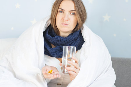 Influenza treatment. Flu-sick woman, wrapped in warm scarf and blanketの写真素材