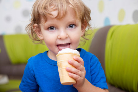 Happy little child in blue t-shirt eating ice cream at homeの写真素材