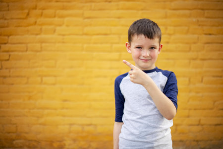 Smiling cute kid pointing with finger aside on yellow brick wall backgroundの写真素材