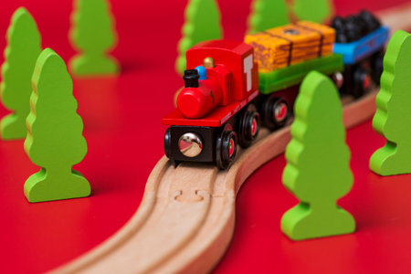 Wooden toy train on the railroad among green trees on red backgroundの写真素材