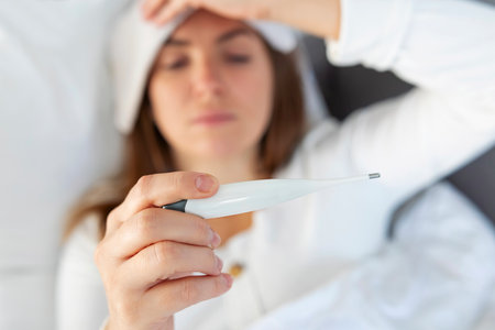 Woman with flu lying in bed, she is measuring her temperature thermometer