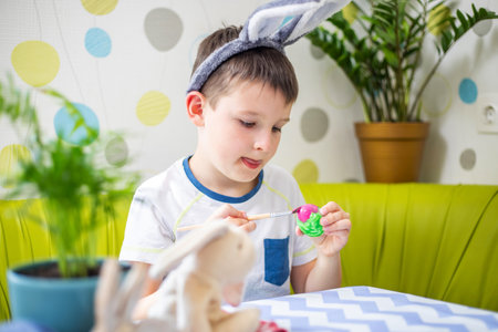 Happy Easter. Boy in bunny ears dyes colorful egg for Easter hunt