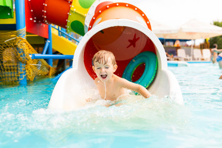 Little boy playing on water slide in outdoor pool on a hot summer dayの写真素材