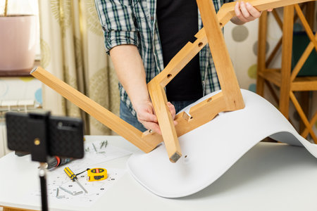 Handyman shows assembling chair, shooting video instructions on smartphone