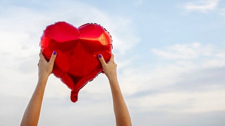 Womans hands with heart shaped balloon on background of skyの写真素材