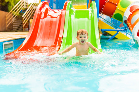 Little boy playing on water slide in outdoor pool on a hot summer day