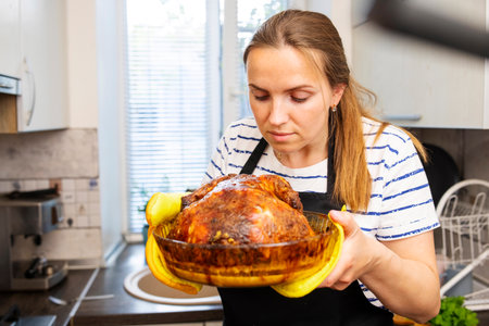 Woman in black apron holding a dish with a roasted chicken in the ovenの写真素材
