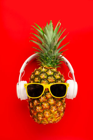 Ripe pineapple with sunglasses and headphones on red backgroundの写真素材