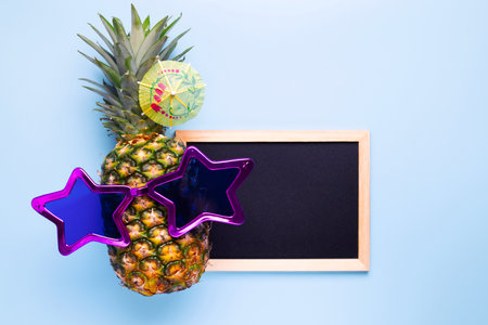 Pineapple in sunglasses with empty blackboard for your text on blue backgroundの写真素材