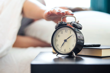 Woman on the bed reaches her hand to turn off the alarm clockの写真素材