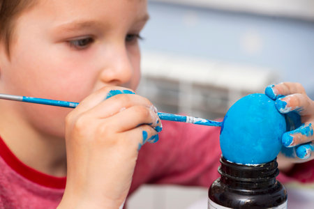 A boy painting Easter eggs at home. A child preparing the easter eggs for Easter