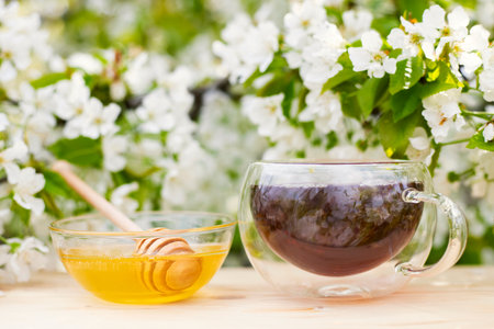 A glass cup of tea with honey in bowl on a wooden table on flowers backgroundの写真素材