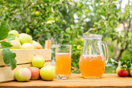 A box of apples and glass and pitcher of fresh apple juice on wooden tableの写真素材