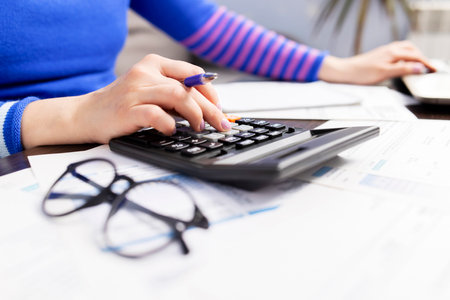 Woman using calculator for calculate domestic bills at home, doing paperworkの写真素材