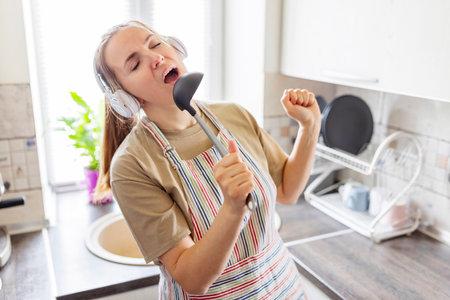 Woman in earphones listening to music and singing while cooking in the kitchenの写真素材