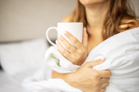 Close up of a woman sitting on bed holding a cup of coffee.の写真素材