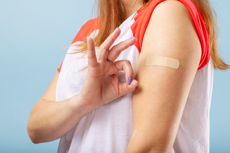 Vaccinated woman is gesturing okay and showing arm with adhesive bandageの写真素材