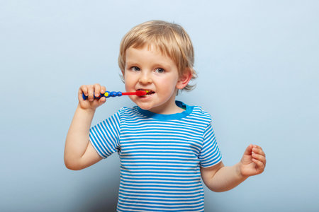 Little blonde boy brushing teeth with toothbrush on blue backgroundの写真素材