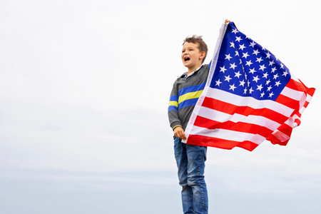 Emotional portrait of patriotic american boy holding USA flag waving in the windの写真素材