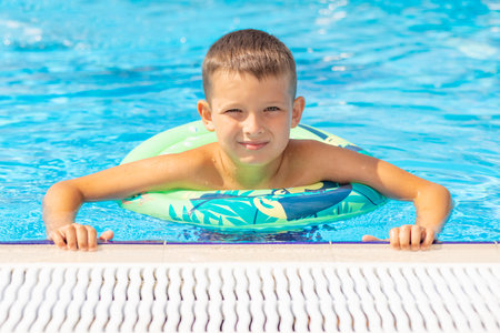 Funny happy child boy in swiming pool on inflatable rubber circle ring.