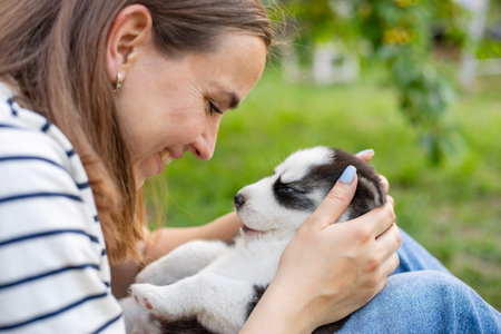 Beautiful woman in striped t-shirt happily plays with small husky puppy in parkの写真素材