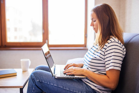 Young woman with a laptop and a cup of coffee on the table at home.の写真素材