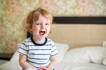 Cute laughing child boy sits in bed. Boy plays at home. Child in a sunny bedroom