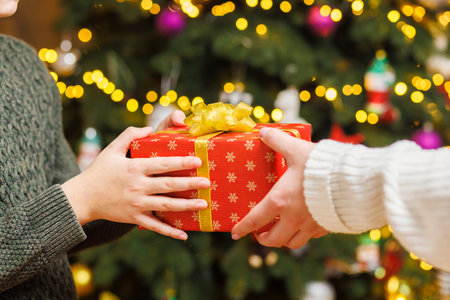 Hands of parent giving Christmas gift to child on Christmas tree backgroundの写真素材