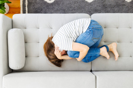 Frustrated woman covering face and crying, lying on sofa at home aloneの写真素材