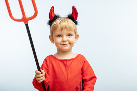 Happy cheerful boy in devil costume with trident on blue background