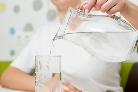 A female is pouring fresh, clear water from a jug into a glass.の写真素材