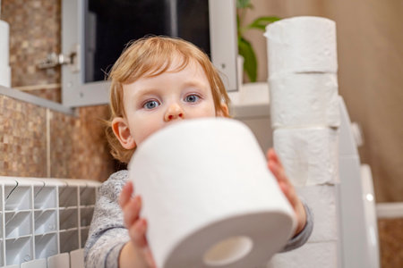 A cute boy is holding toilet paper roll in bathroom. Young boy with toilet paperの写真素材
