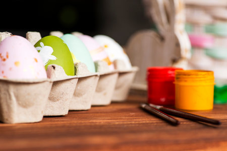 Colorful easter eggs, multi-colored paints and brushes on wooden table.