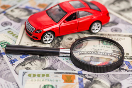 Magnifying glass and toy red car on dollar bills background.の写真素材